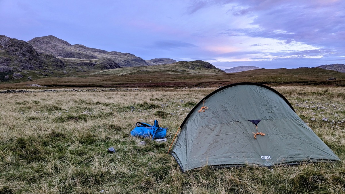 Camping at Eskdale with my tent in the foreground, and mountains in the background in front of a dramatic sunset