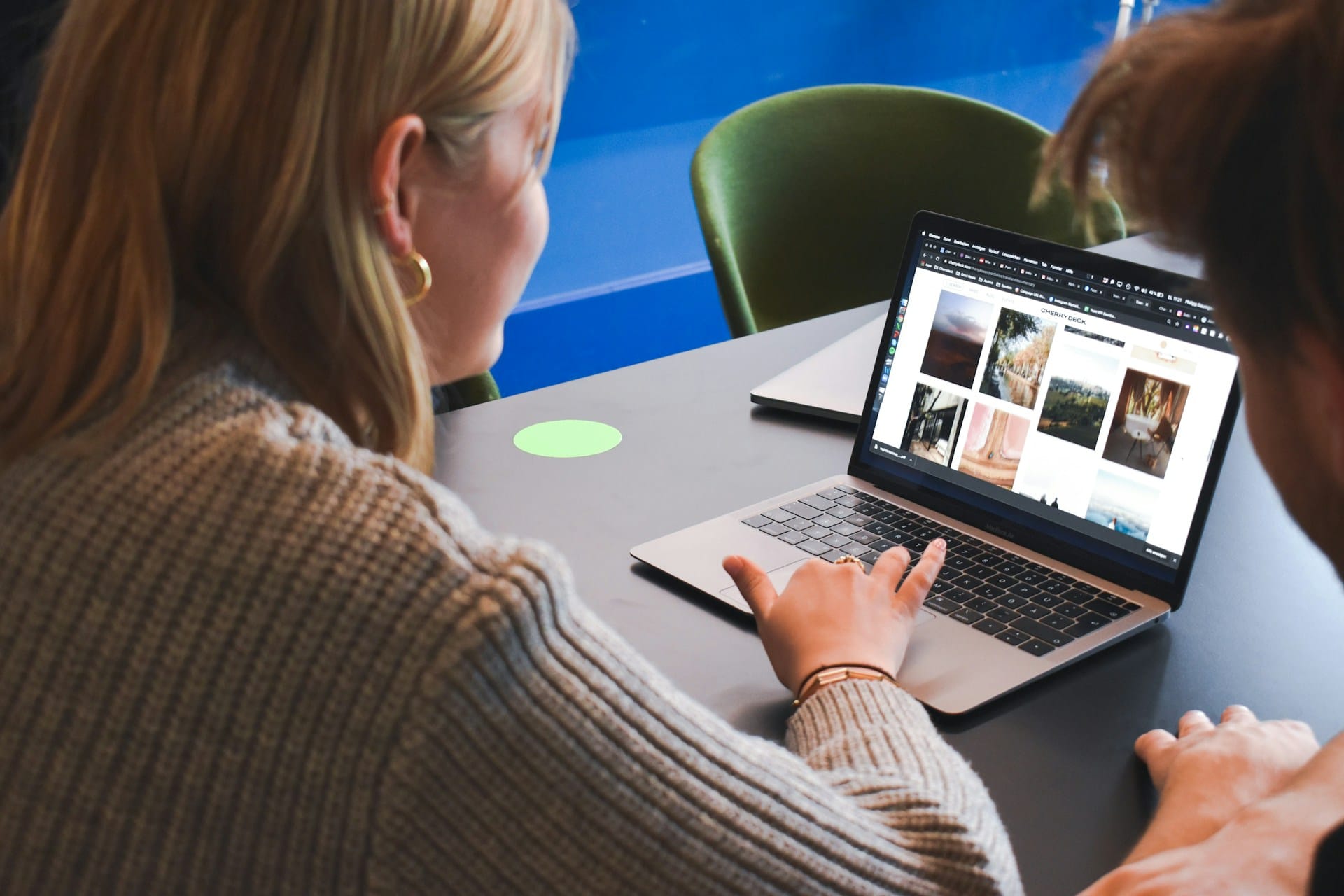Woman in grey sweater using laptop while someone else looks on