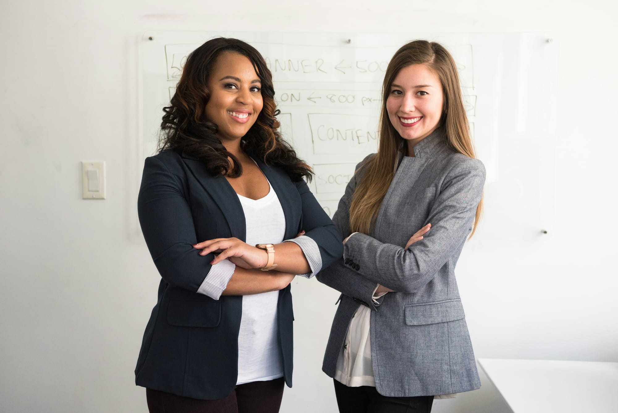 Two women in suits standing beside a whiteboard
