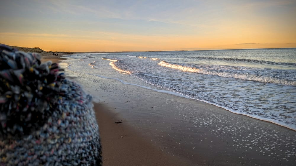 A woolly hat in the foregound with a sunset beach in the background 