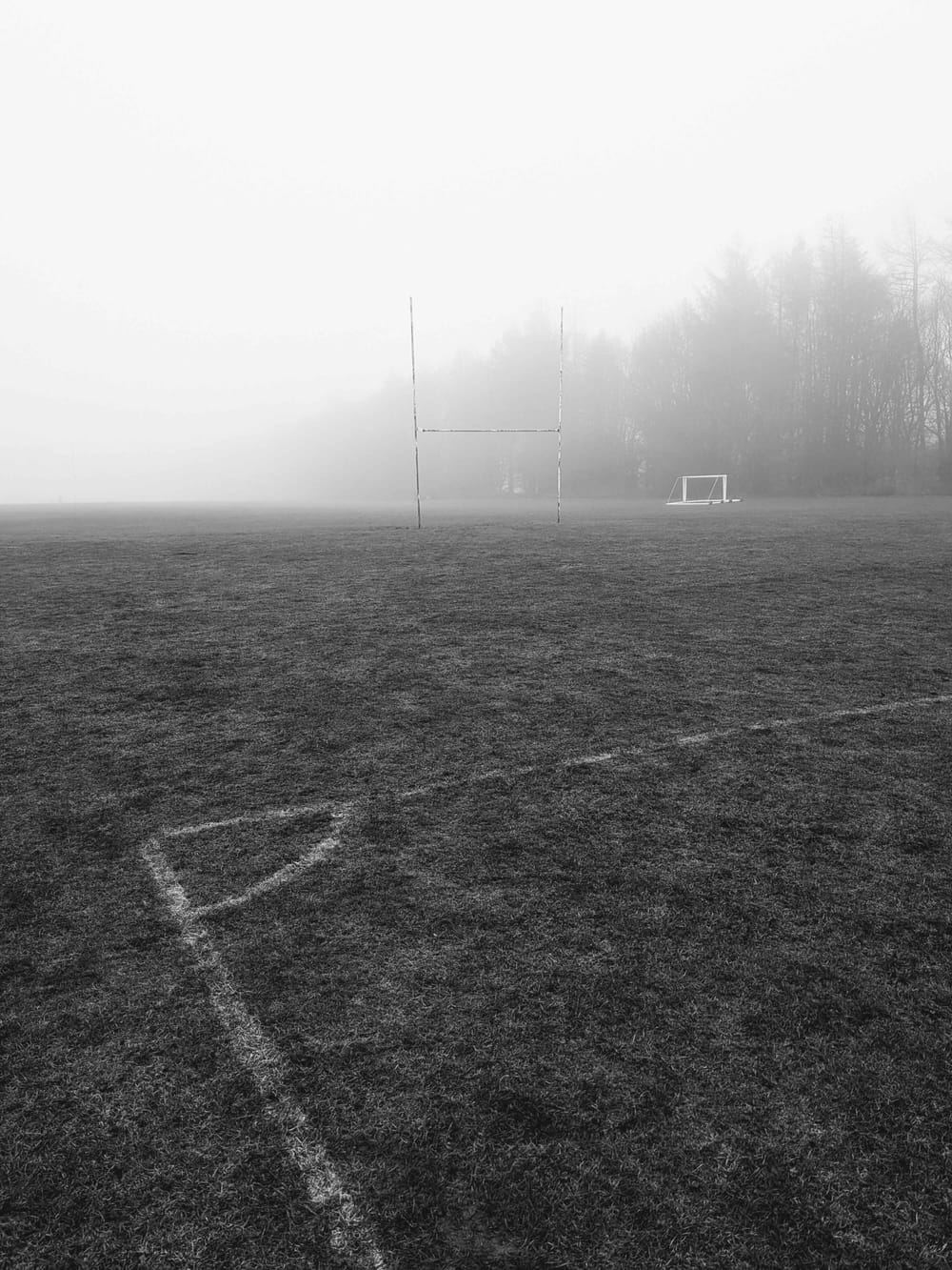 Corner of a football pitch, with rugby posts, trees, and fog in the distance