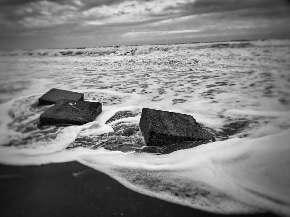 Black and white photo of roiling sea around concrete WW2 anti-tank blocks 