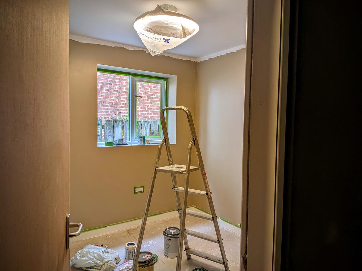 Looking into Doug's new home office which contains a ladder and some tins of paint. The walls are almost finished being painted.