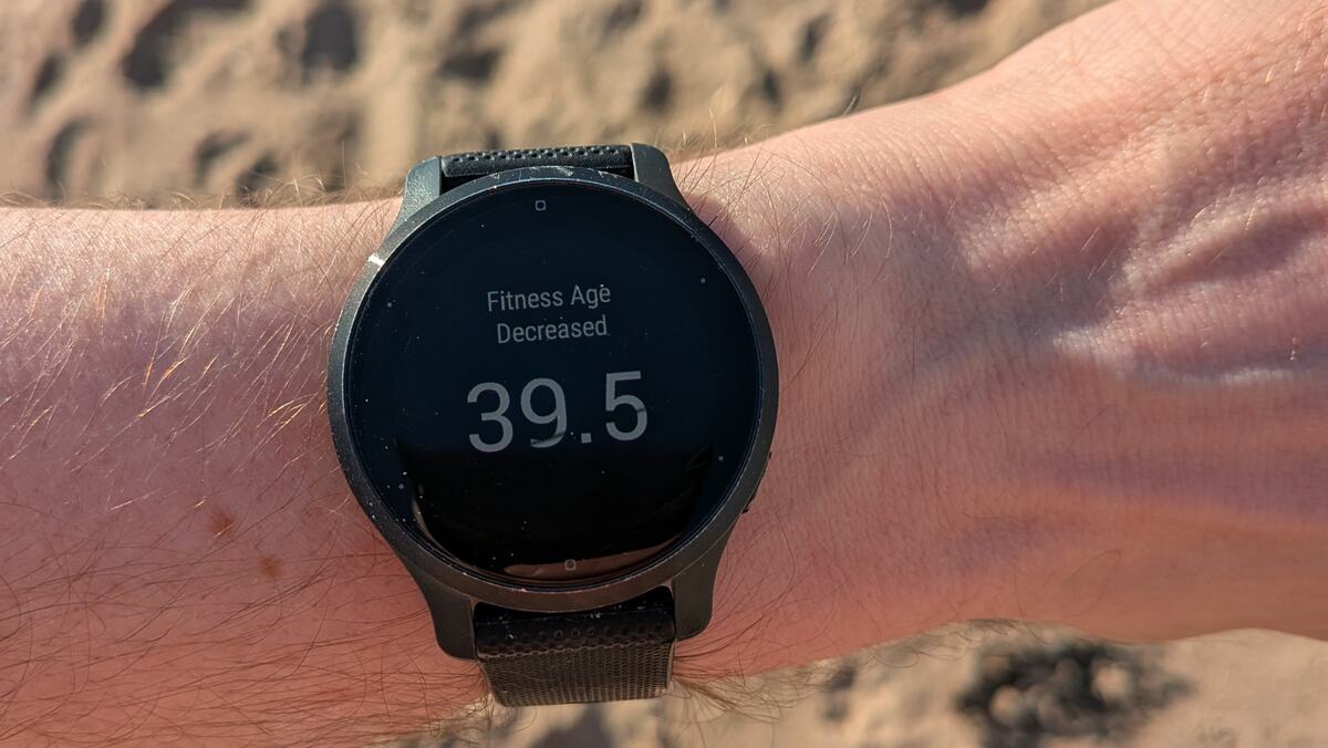 Photo of watch on wrist with sand in background. The watch face says "Fitness Age Decreased 39.5"
