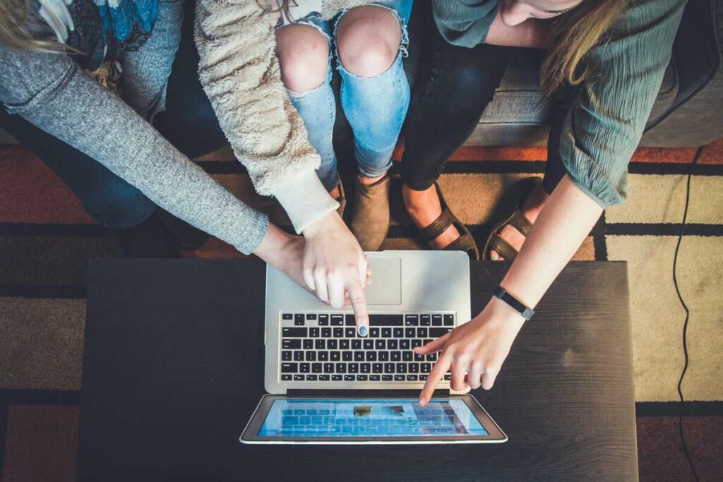 Top-down view of three people pointing at a laptop screen on a dark wooden table.
